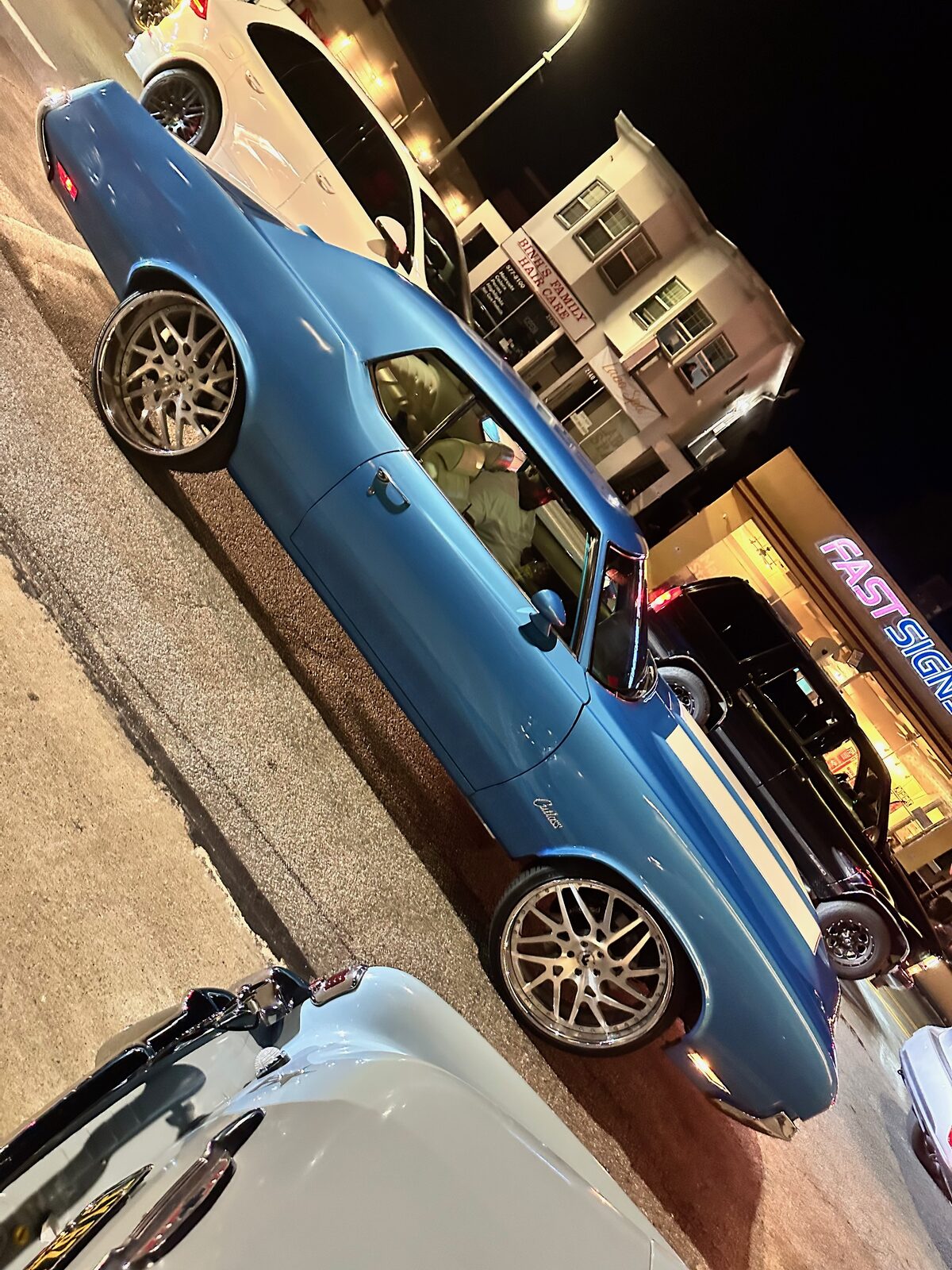 A blue coupe with polished wheels parked under streetlights at night