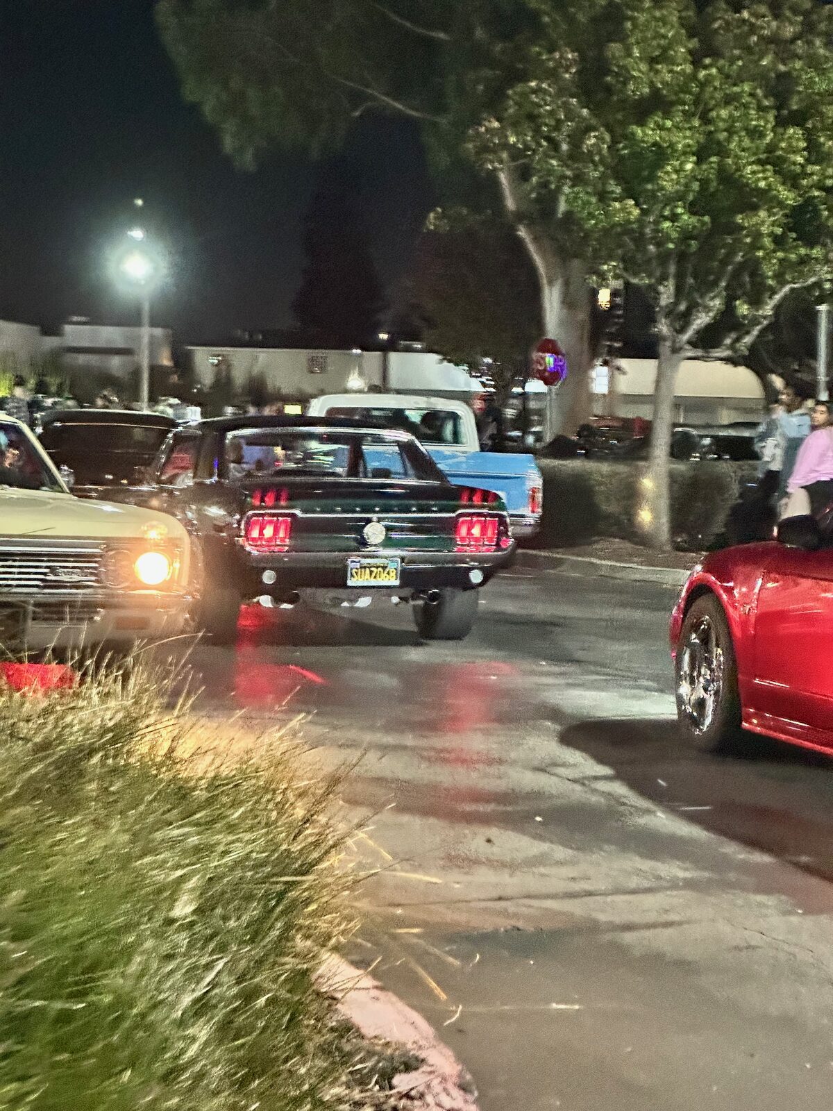 Tail lights of a Mustang at night with a crowd of people watching