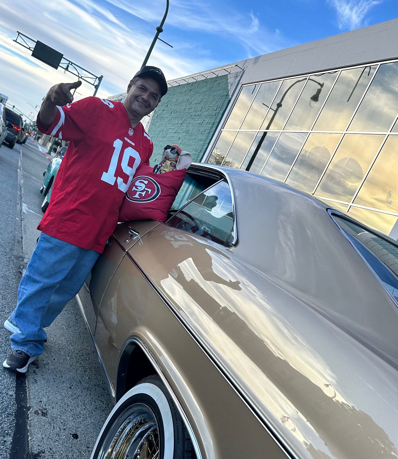 A man in a red San Francisco 49ers jersey giving a thumbs up beside a gold lowrider