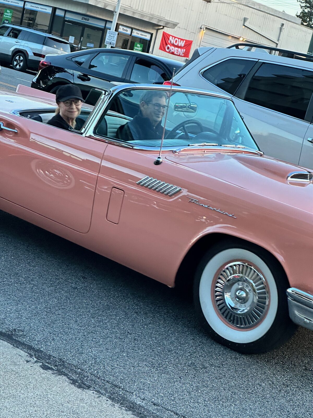 A couple sitting in a pink 1957 Ford Thunderbird, both smiling