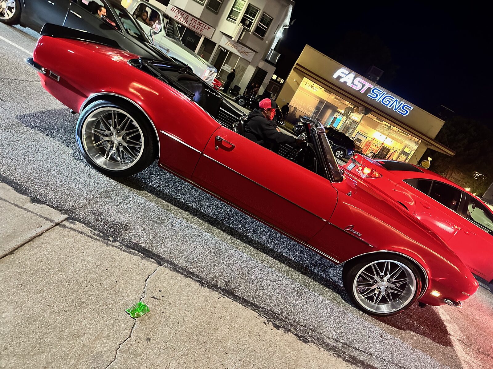 A red convertible at night glowing under a lit storefront sign