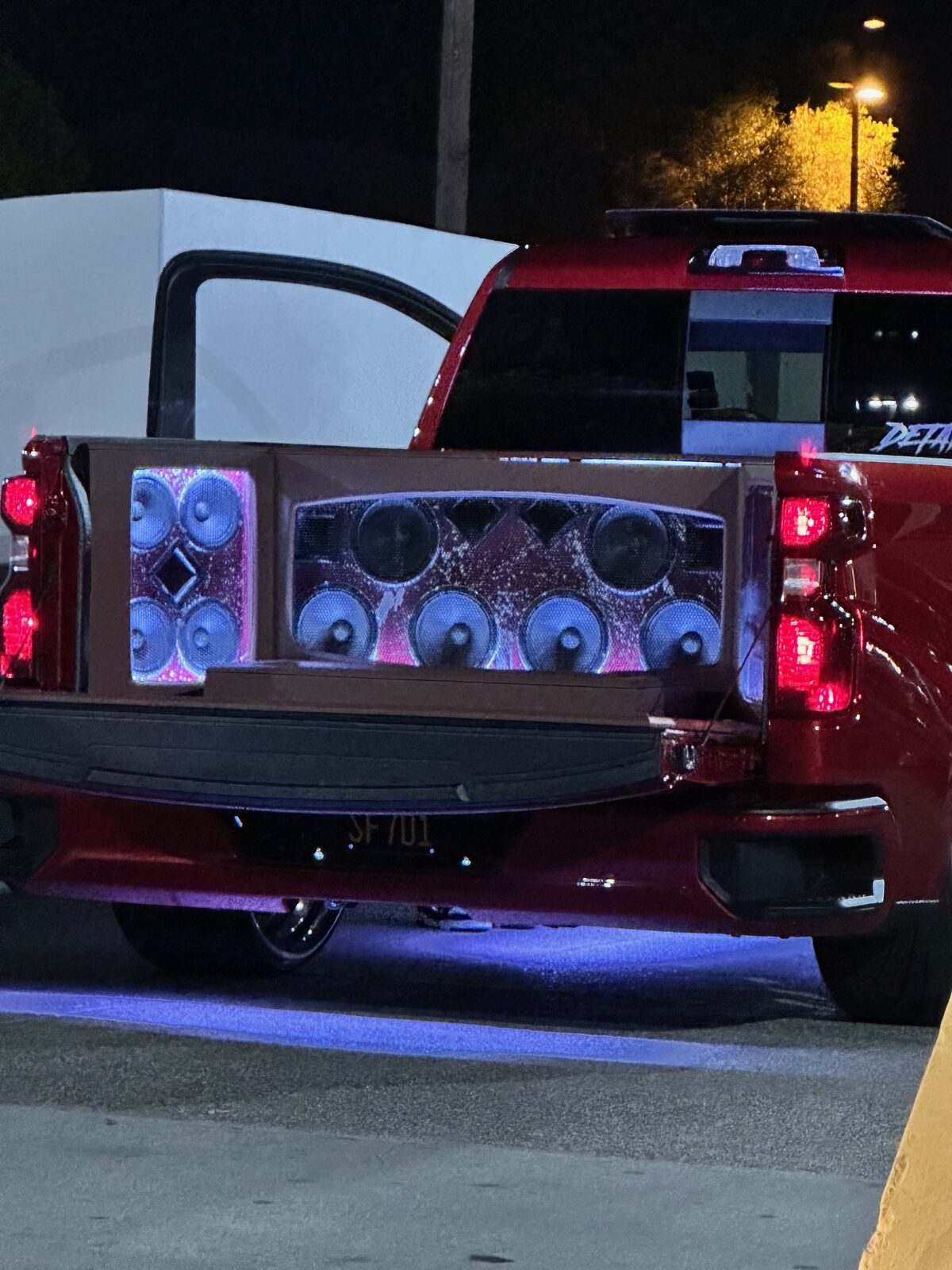 A truck with a wall of speakers in the bed and purple underglow lighting